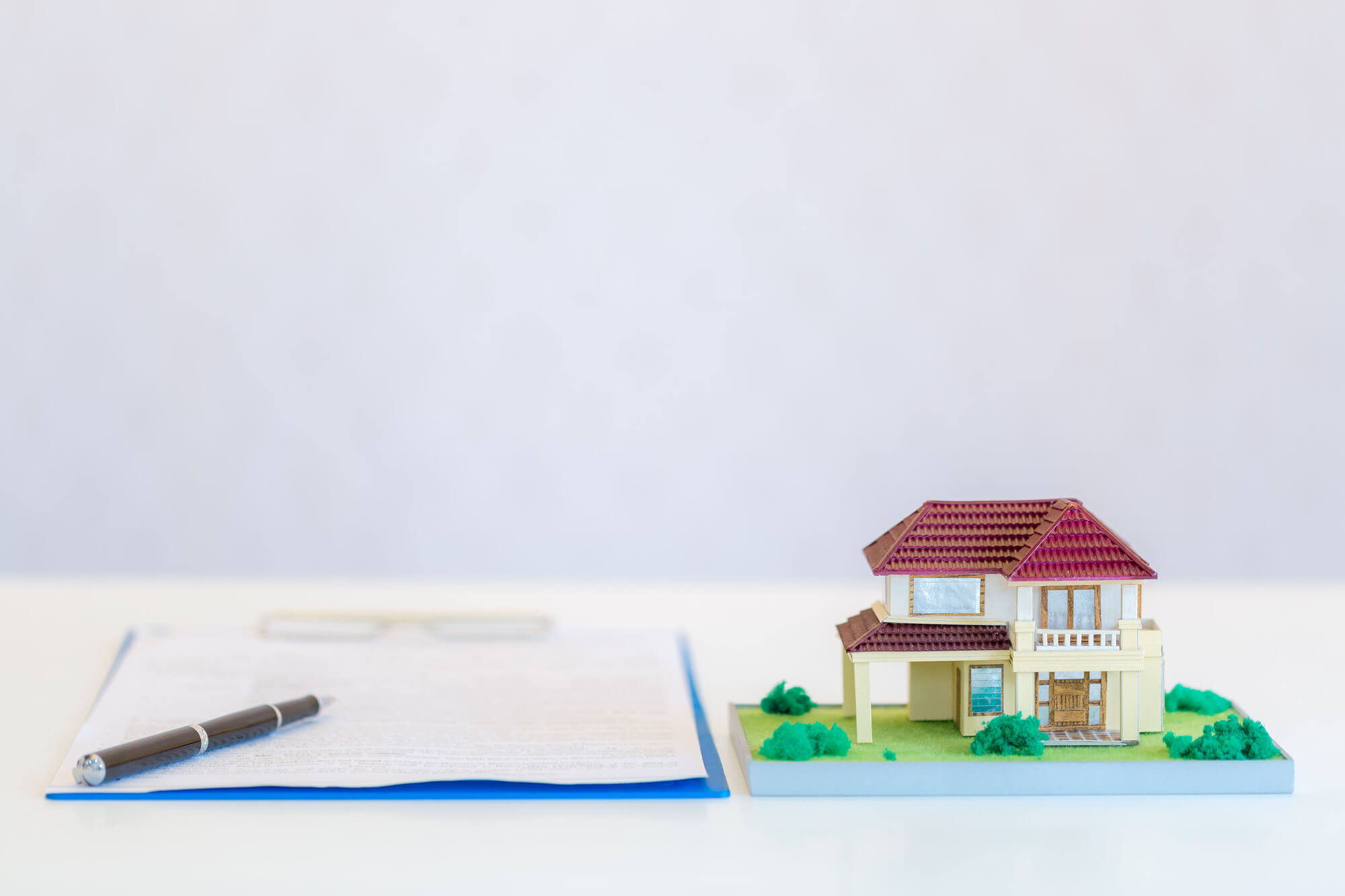 Imagem de um contrato com uma miniatura de casa.